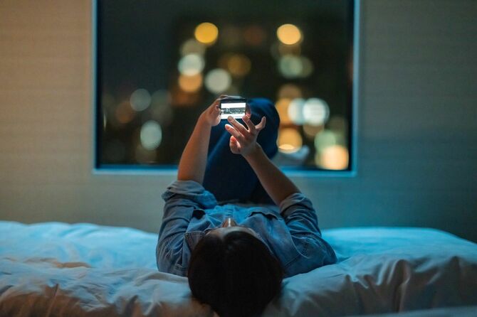 ベッドに横たわりスマートフォンを使用する女性