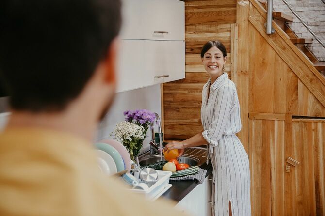 キッチンで野菜を洗いながらパートナーと笑顔で話す女性