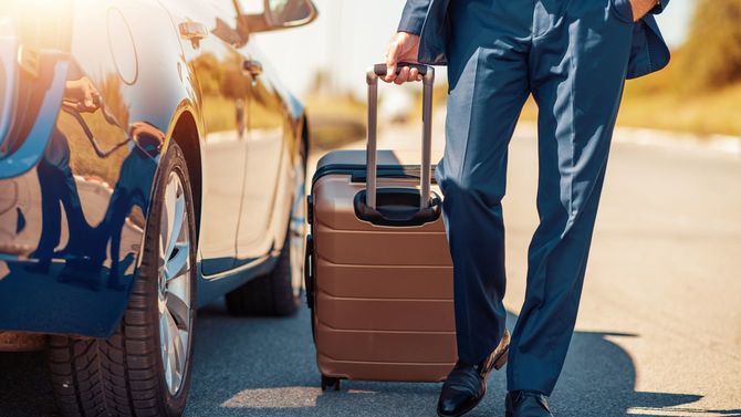 スーツケースを持った旅するビジネスマンが車の横に立っている