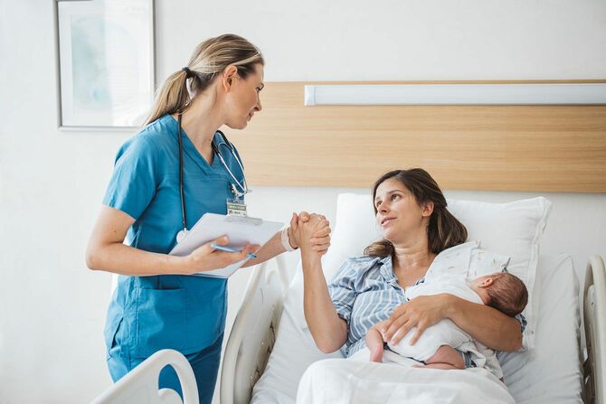 病院のベッドで赤ちゃんを抱き、看護師の手を握る母親