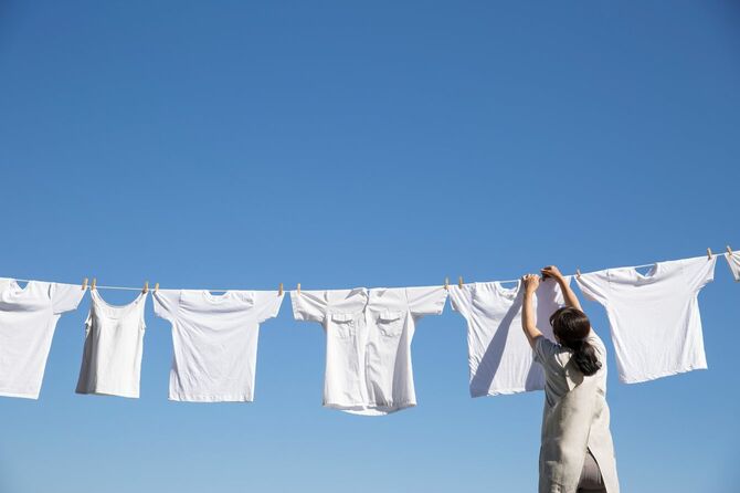 青空の下洗濯物を干しているエプロン姿の女性