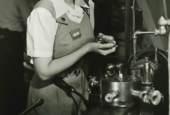 オーバーオールで働く若い女性が旋盤で工場