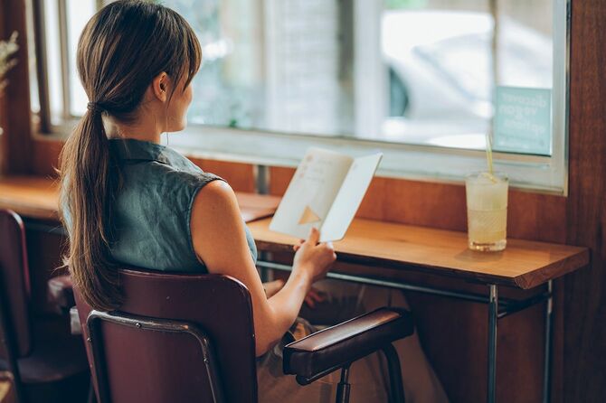 カフェに座って、彼女のノートボクからノートを読む学生