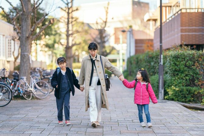 働く母親が娘たちと手をつないで一緒に通りを歩いている