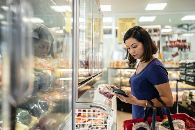 スーパーで肉を手にスマホで調べ物をしている女性