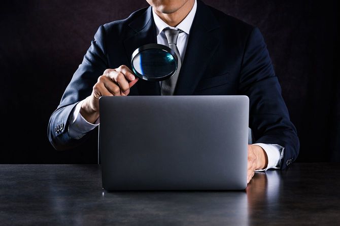 拡大鏡でラップトップコンピュータを見ているビジネスマン
