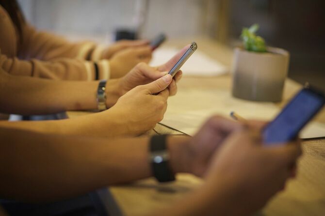 同じテーブルについている人々がそれぞれの手に持つスマホに目を落としている