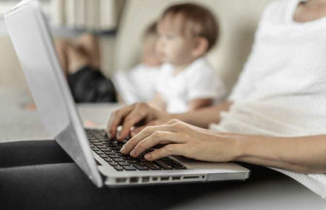 ノートパソコンを使用して在宅勤務している母親のそばには子供たち