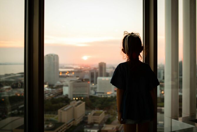 アパートの窓から夕日を眺めている少女