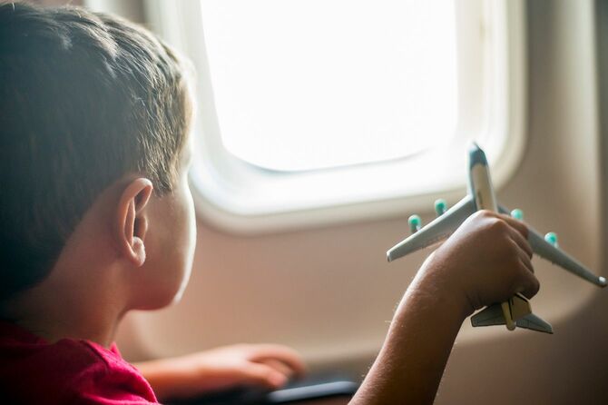 窓の外を見ながら飛行機で旅行中におもちゃの飛行機で遊んでいる少年