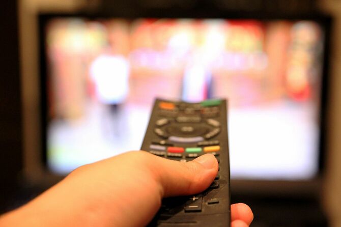 テレビにリモコンを向けてボタンを押している手元