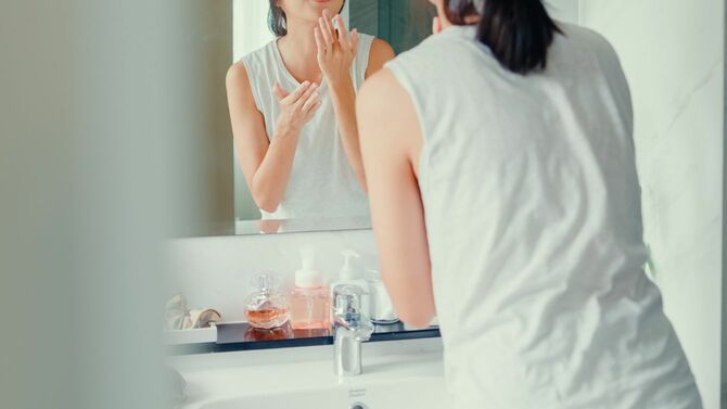 洗面所で顔にクリームを塗っている女性