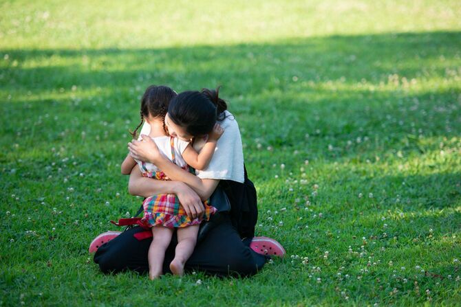 公園の原っぱで娘を抱きしめる母親