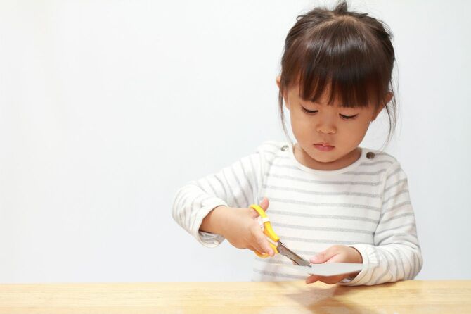 3歳の女の子がハサミで紙を切っている