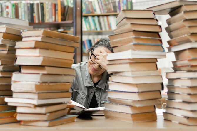 うず高く積まれた本の間で、笑顔で読書をしている女性