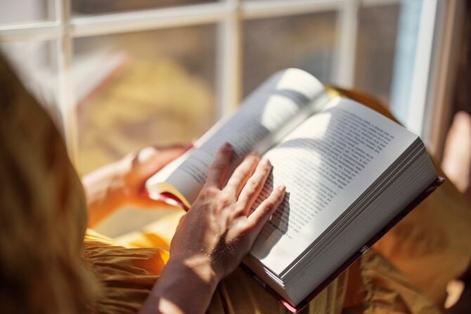 窓辺に座って本を読んでいる女性の手元