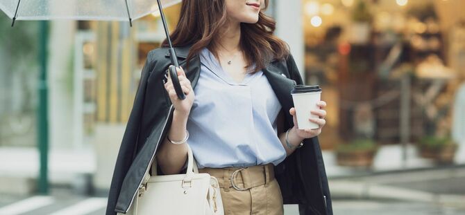 コーヒーを手に傘をさして歩く女性