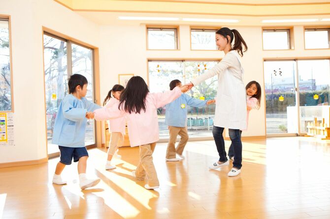幼稚園で、園児と輪になって踊る保育士