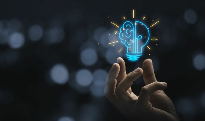 半分が脳の形が描かれた、イラストの電球を持っている手