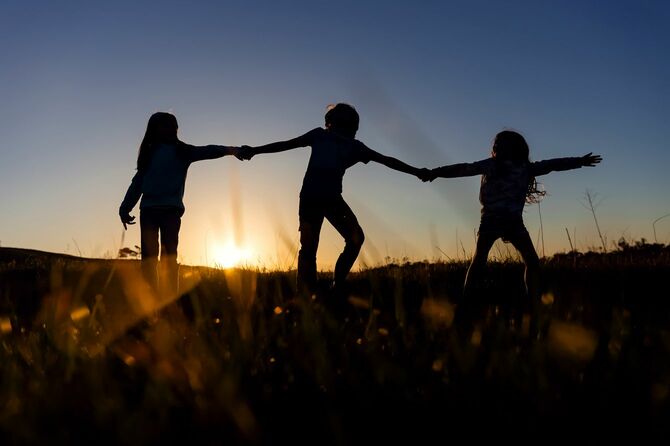 夕暮れ時の原っぱで手をつないで遊ぶきょうだいのシルエット
