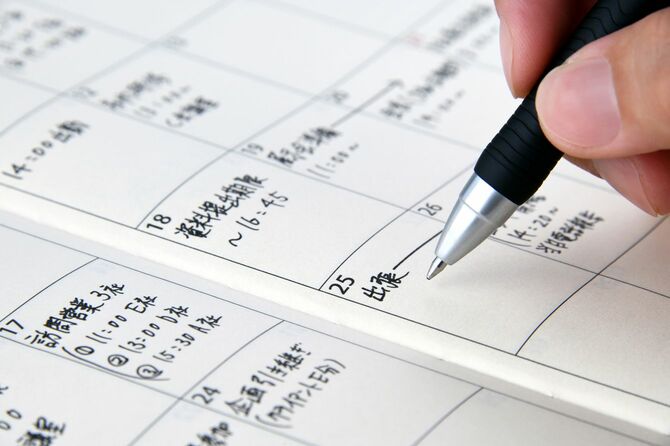 紙の手帳にスケジュールを書き込んでいる手元