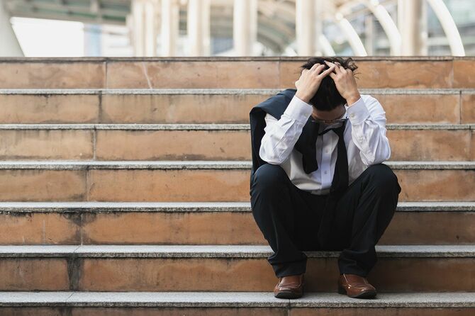ストレスを抱えた若いアジアのビジネスマンは、階段に座って頭に手を合わせていた。失業とレイオフの概念。
