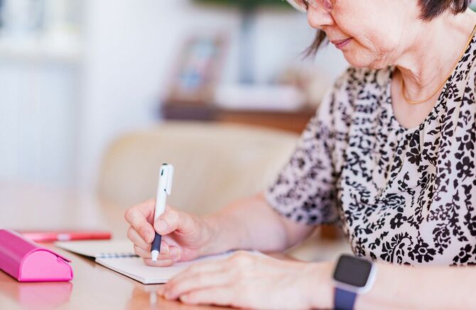ノートにメモを書く高齢の女性