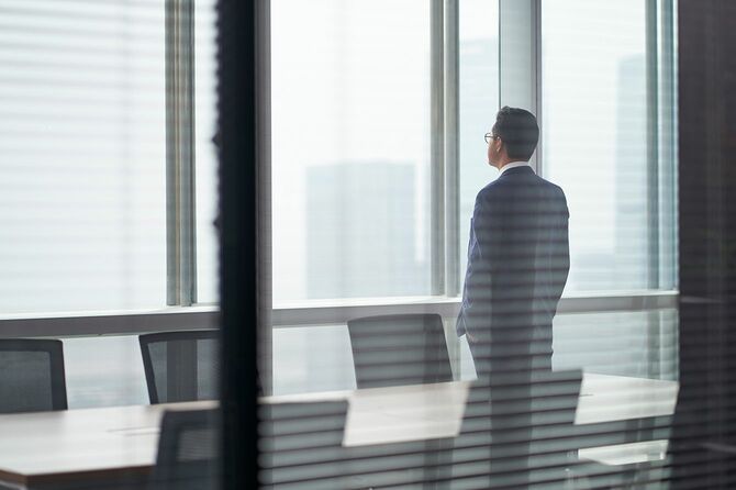 オフィスの窓の前に立ち、外を見てポケットに手を入れた考えを持つアジア人ビジネスマン