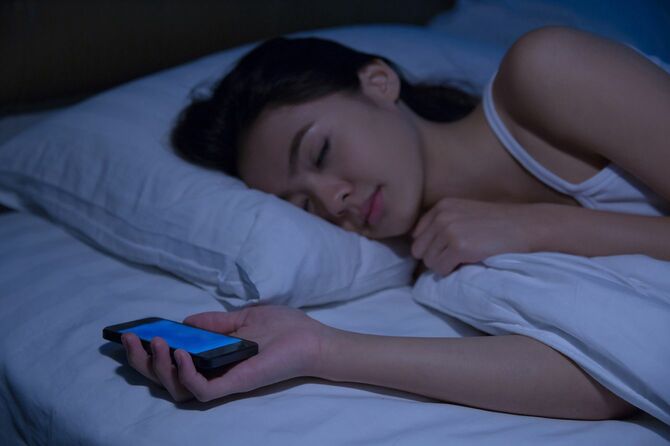 アジアの女性は、夜に眠っている彼女の前にベッドの上、スマート フォンを使用しています。