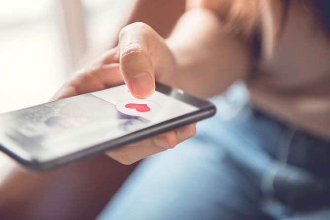 スマホ画面に表示されたハートマークを押す女性の手元