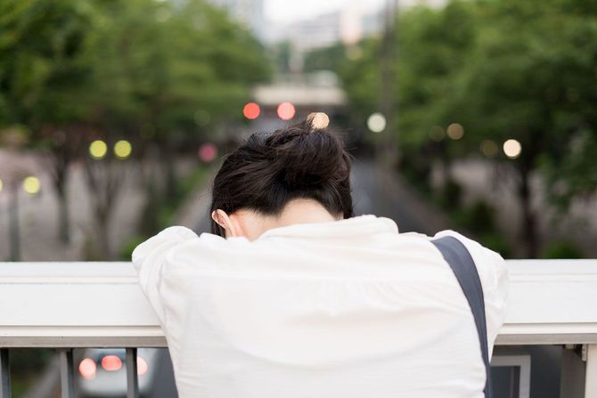 歩道橋の手すりに顔をうずめて落ち込んでいる女性