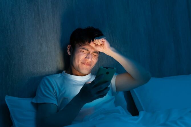 夜にベッドでスマートフォンを触る男性