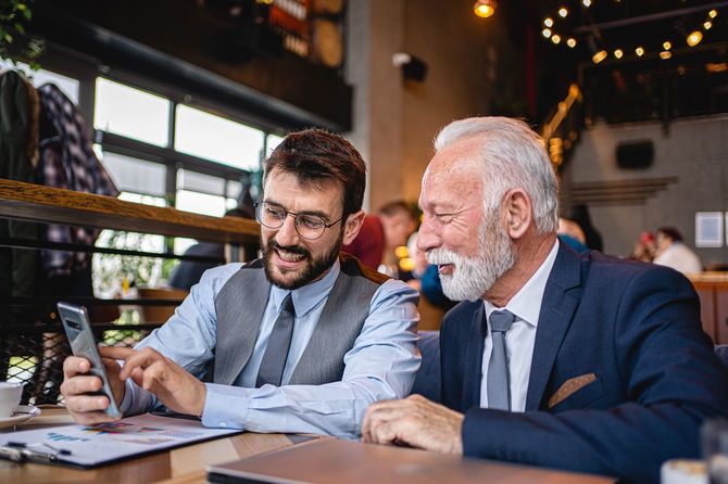 コーヒーショップでスマホを見ながら話をするシニアビジネスマンと彼の同僚