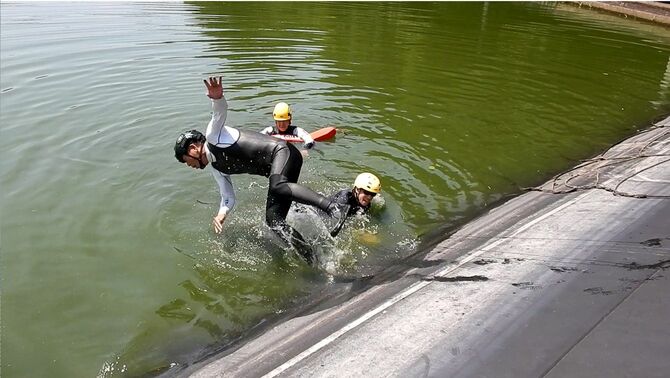 和歌山県広川町で行われた、ため池管理者向け安全研修会の様子。ため池に落ちた人を助けようとして、自分も落ちてしまう様子を実演した（2023年7月撮影）