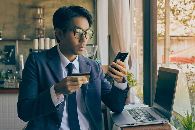 クレジットカードを持ちながらスマホを使用するビジネスマン