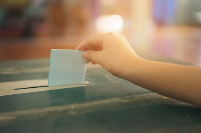 投票ボックスで選挙投票の概念のための投票用紙を保持するクローズアップハンド