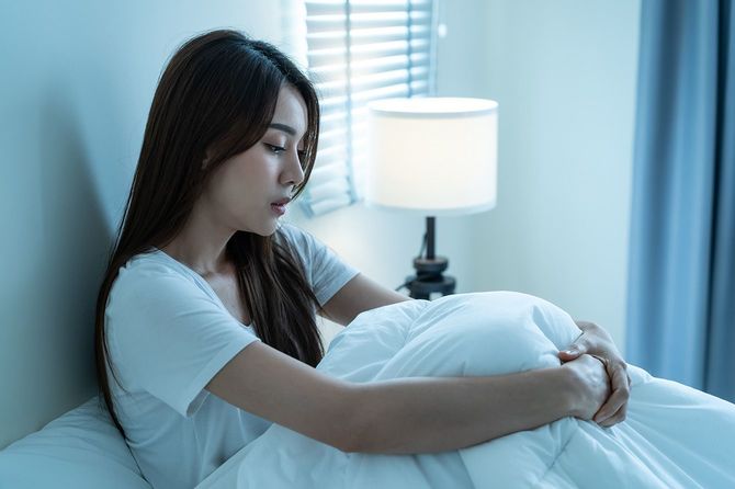 ベッドの上で膝を抱えて座っている女性