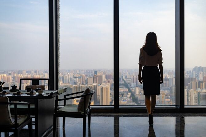 高層階のオフィスの窓際に立つ女性