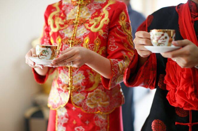 中国の茶道にティーカップを持つ伝統的な結婚式の衣装で花嫁と花婿