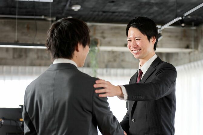部下の肩に手を置いて笑顔で話す上司
