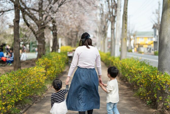 桜の通りを歩く母親と2人の子供の背面図