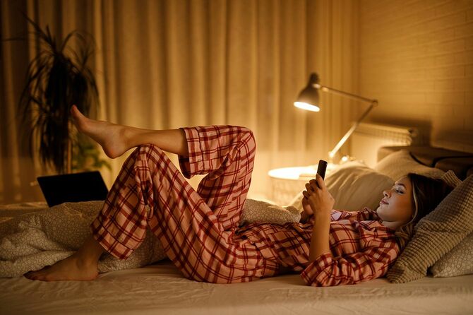 ベッドの若い女性は夜に携帯電話を使用しています