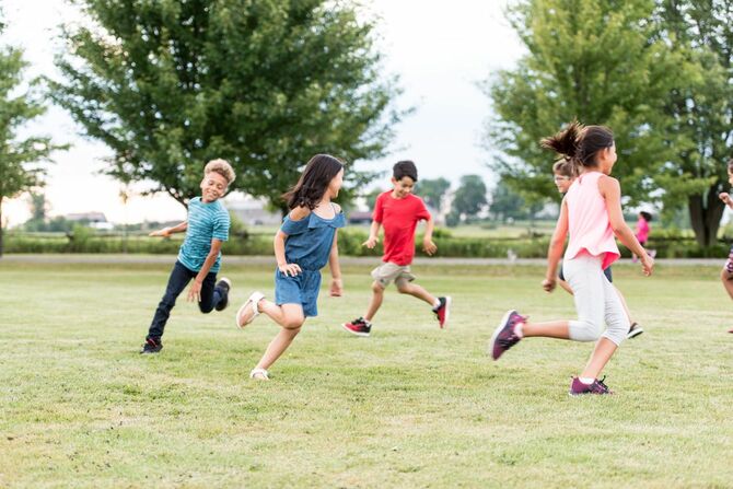 学校の外の芝生を走り回る小学生たち