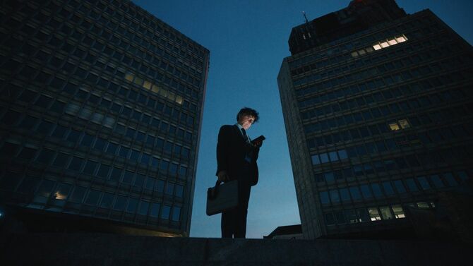 明かりも消えつつあるビルの谷間に立ち、スマホに目を落としている中年のビジネスマン