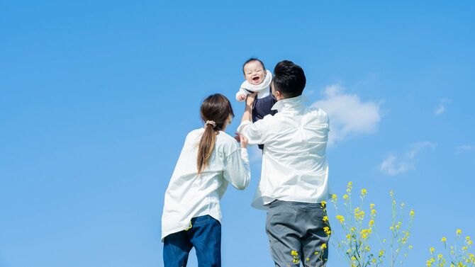 青空の下、赤ちゃんを高い高いする若い夫婦