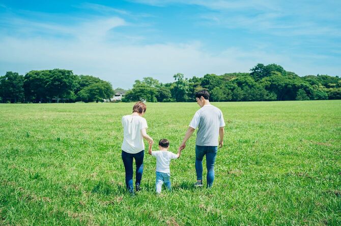 親と子が手をつないで、日当たりの良い緑地を歩く