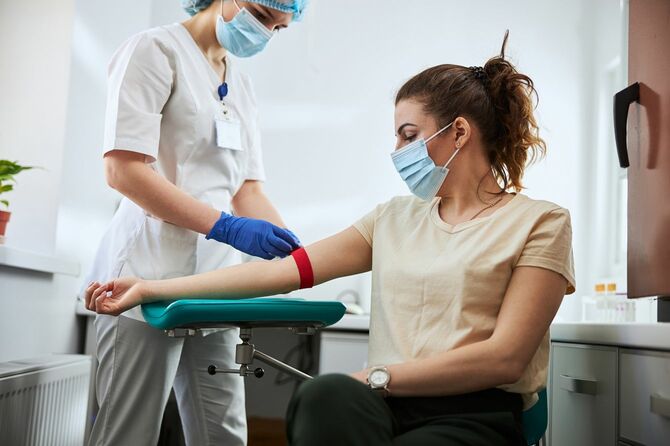 採血のため、女性患者の腕に止血バンドを装着する熟練した若い医療従事者