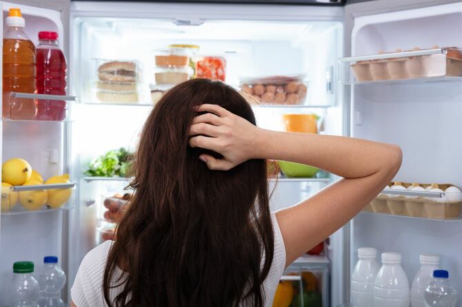 冷蔵庫を開けて悩む女性