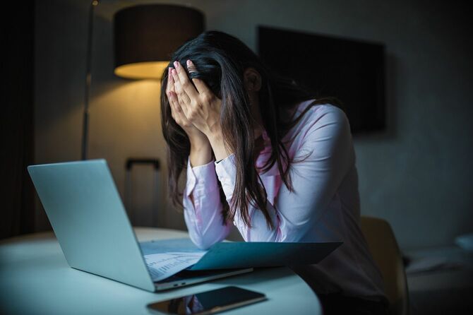 広げたノートパソコンと書類の前で苦しんでいる女性