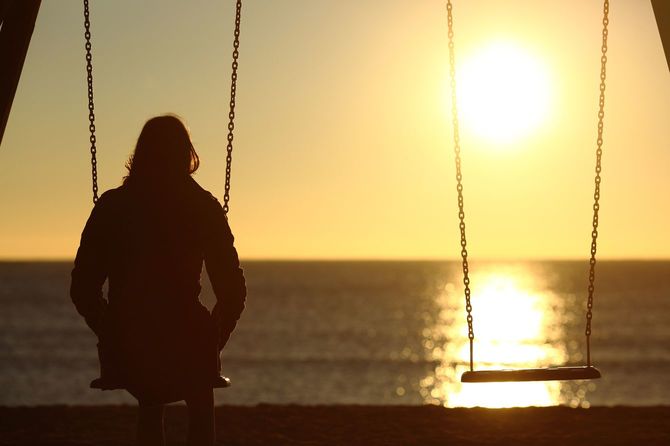 一人寂しく冬のビーチのブランコに腰掛ける女性